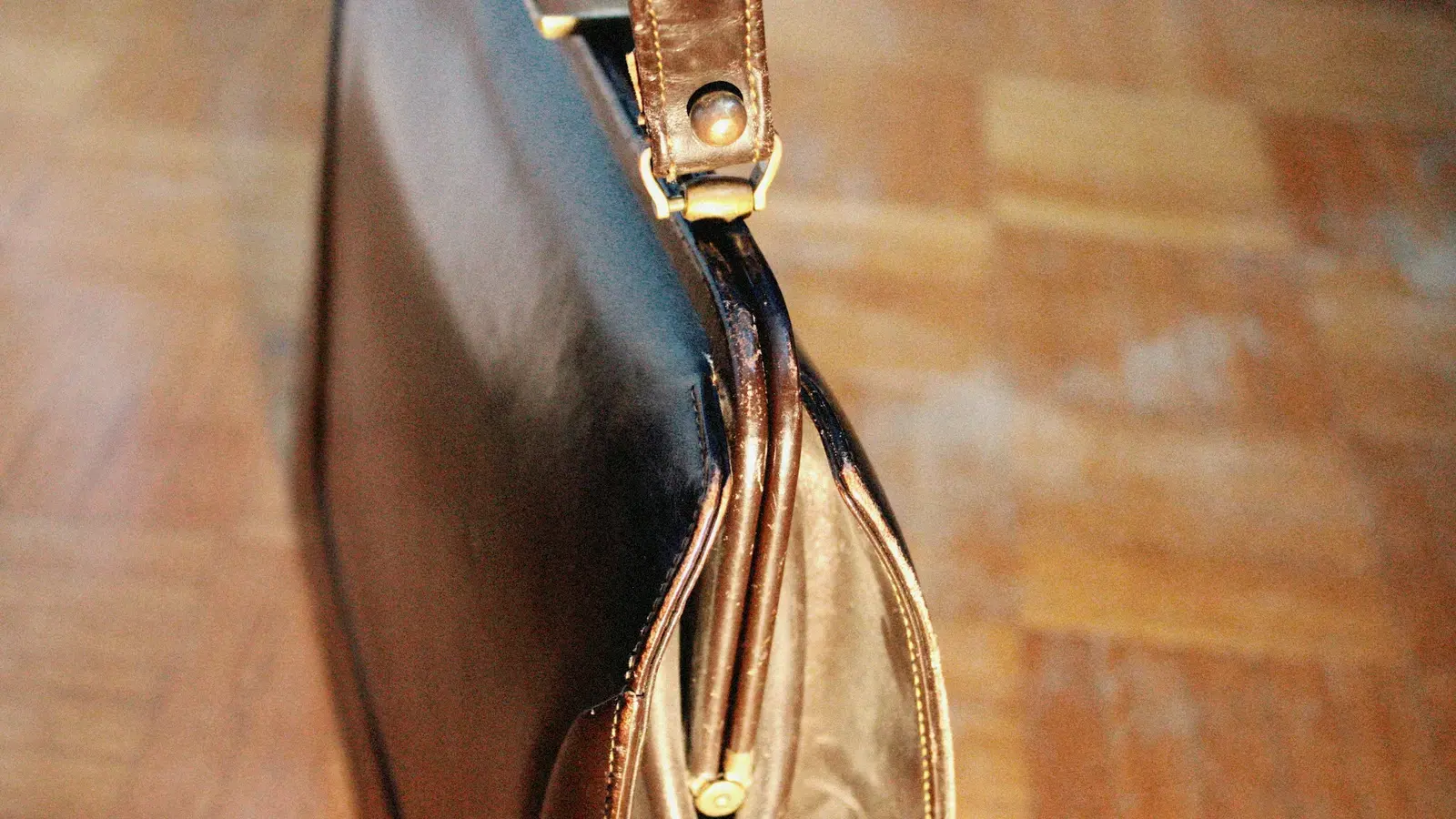 木の床に置かれた、黒い革のバッグの側面と金具